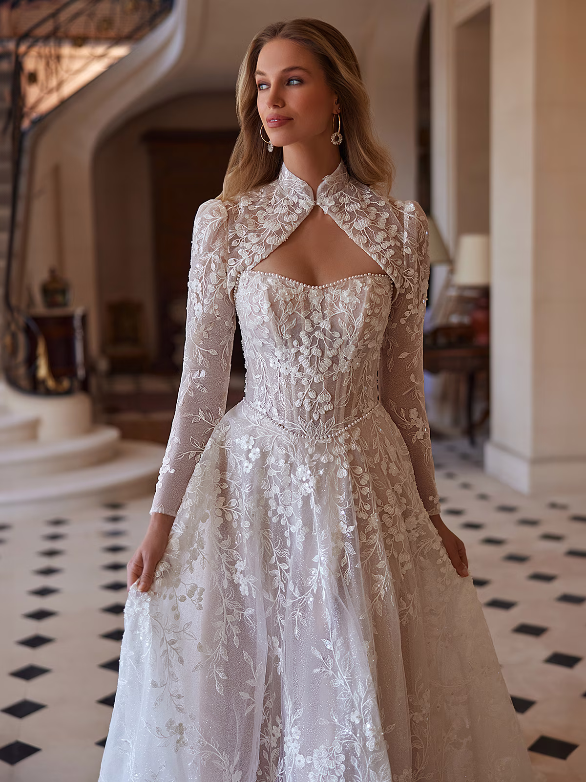 Woman looking away to the side, wearing a beaded lace A-line with detachable Bolero jacket with long sleeves.