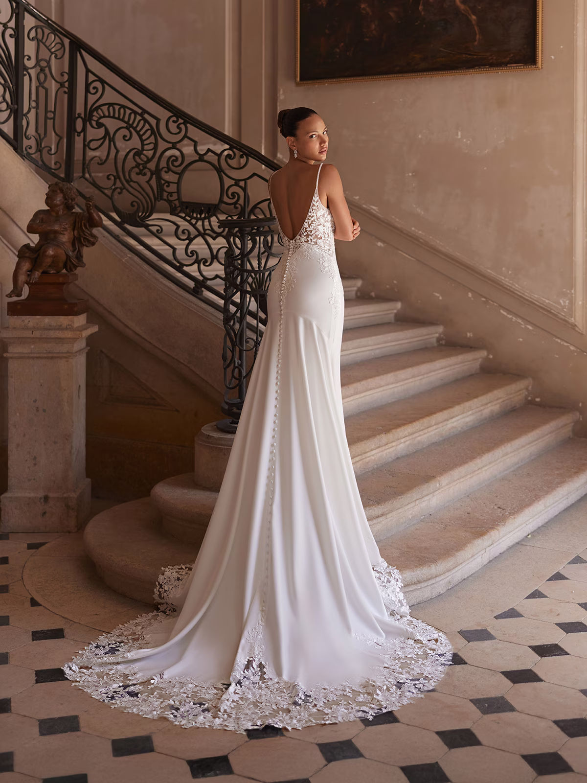 Tall bride in a crepe wedding dress standing next to an iron railing and marble staircase