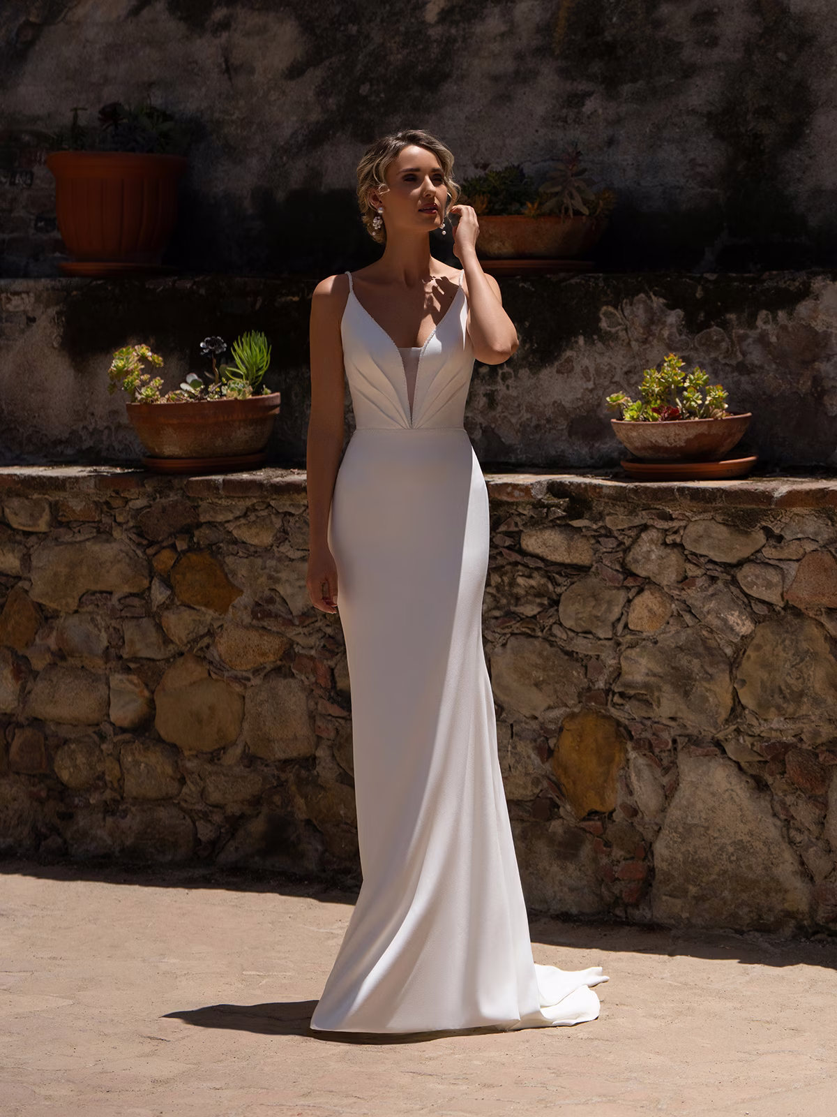 Bride standing in a courtyard wearing a crepe wedding dress with beaded spaghetti straps